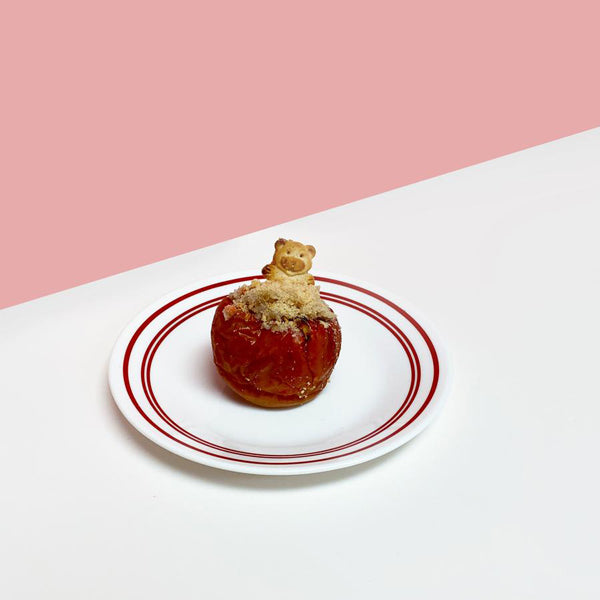Baked Apple stuffed with food and topped with a treat sitting on a plate with pink and white background.