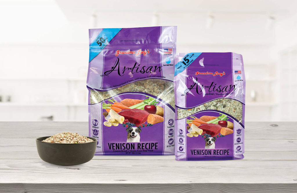 Two sizes of Grandma Lucy's freeze-dried artisan venison food packages arranged on a kitchen table with filled dog bowl placed by the bags.