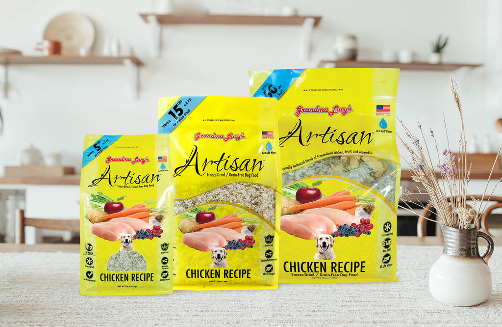 Three sizes of Grandma Lucy's freeze-dried artisan chicken dog food packages arranged on a kitchen table.