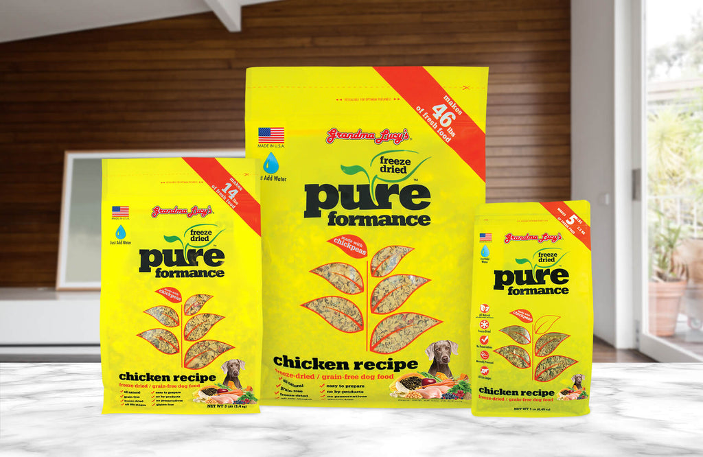Three sizes of Grandma Lucy's freeze-dried Pureformance chicken dog food packages arranged on a kitchen table.
